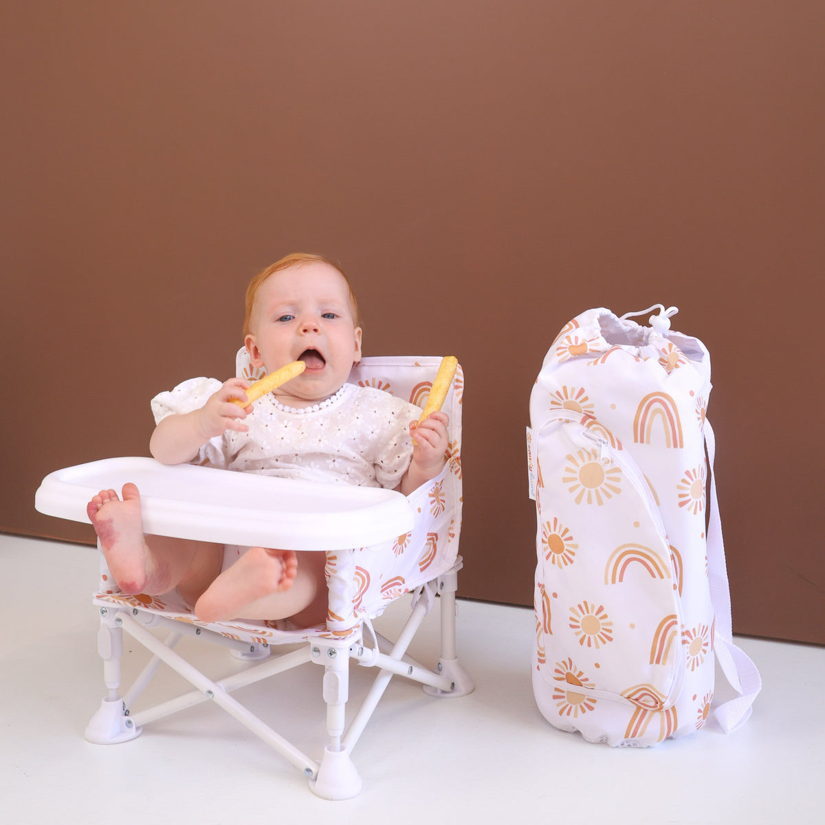 Baby sitting in a high chair with a bag of toys next to them on a brown background